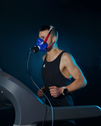 Person on a treadmill wearing a blue respiratory mask in a dark setting