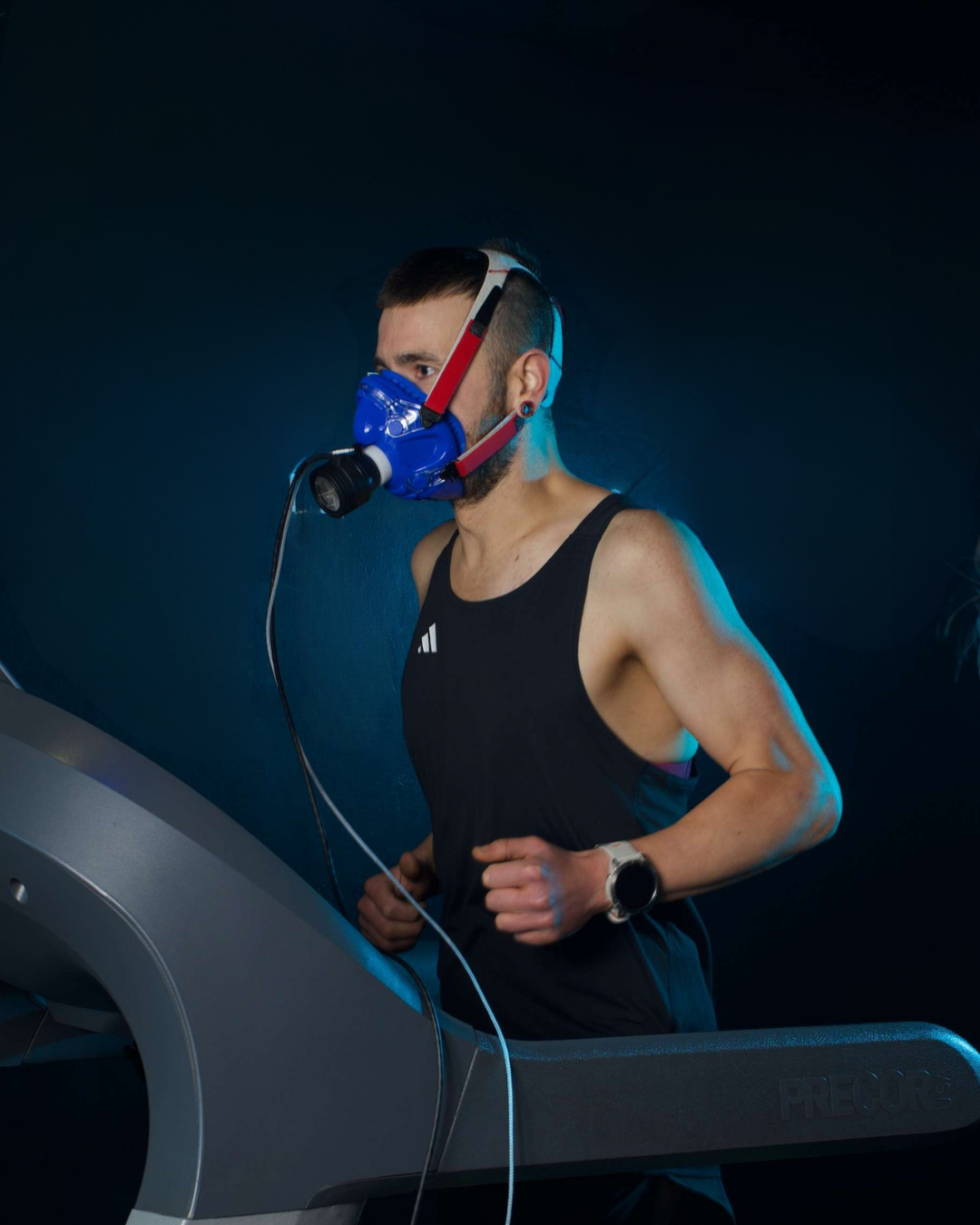 Person on a treadmill wearing a blue respiratory mask in a dark setting