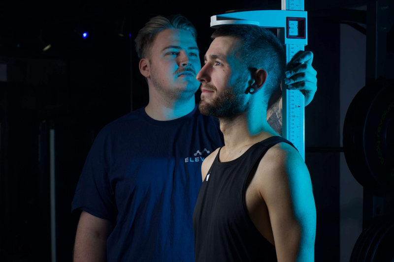 Two men standing in a dark room with one holding a blue measuring device.