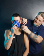 Person adjusting a blue mask on another person against a dark background