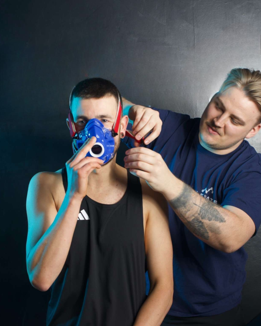 Person adjusting a blue mask on another person against a dark background